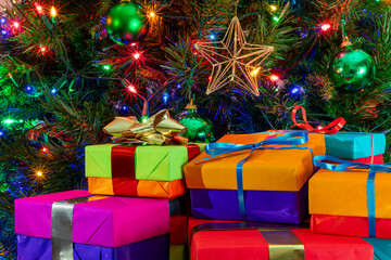 Pile of Colorful Wrapped Gifts Beneath Christmas Tree with Ornaments and Sparkling String Lights