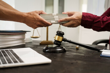 A male lawyer works at his desk, receiving cash from a client while considering the case. He focuses on law, justice, fairness, and the observance of legal rules and conventions in the system