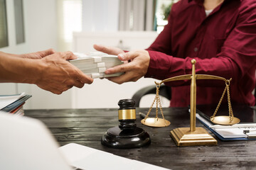 A male lawyer works at his desk, receiving cash from a client while considering the case. He...