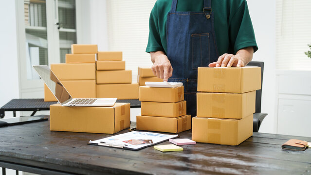 A man is working at his desk, preparing parcel boxes for shipment. He checks and packs items carefully, using shockproof materials, and attaches labels before sending them to customers via EMS.