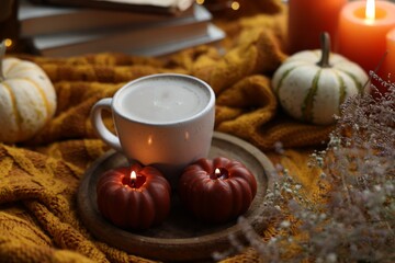 Cup of coffee and burning pumpkin shaped candles on soft sweater. Autumn atmosphere