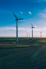 Aerial scenic view of renewable windmills turbines supplying cultivation area with eco power getting energy from wind blowing on vast area of agriculture meadows next to sea. Alternative electricity