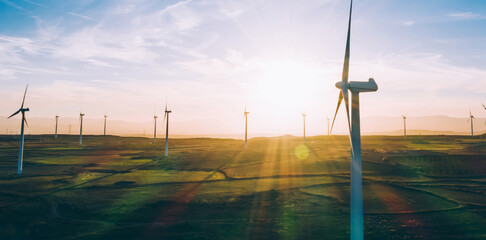 Modern windmills with rotating propellers standing in rural farmland agri meadow over orange sunset...
