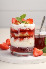 Tasty trifle dessert. Strawberries, sponge cake and whipped cream in glass on beige table