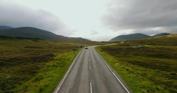 Cinematic panoramic view of white traveler car driving with epic Scottish views on famous North Coast 500