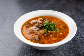 A bowl of soup with a piece of meat in it