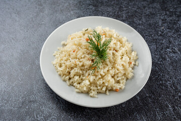 A white plate of rice with a green herb on top