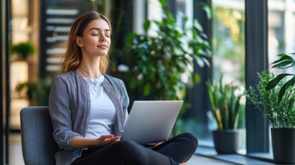 Woman sitting in office with laptop, engaged in focused work or relaxation.