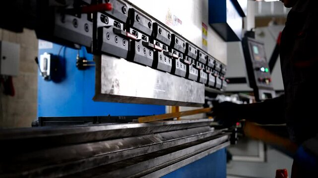 Man working with sheet metal on CNC hydraulic press brake. He puts the part and bends it into a large machine at an angle