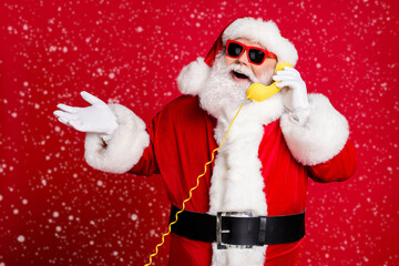 Portrait of nice handsome cheerful cheery bearded Santa father answering calls discussing event consultation service call center operator isolated bright vivid shine vibrant red color background