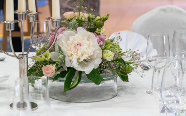 Floral wedding decoration. Served wedding table with fresh flower, candle holders. Details of celebration. Floral arrangement, glass, candle in candlestick.