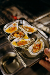 Grilled oysters with cheese and spices on a serving tray, ideal for food menus, seafood promotions