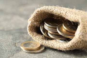 Euro coins in burlap sack on grey table, closeup