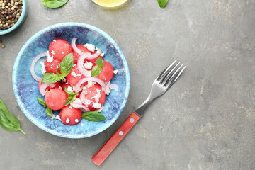 Delicious watermelon salad with feta cheese, mint and onion in bowl served on grey textured table, flat lay. Space for text