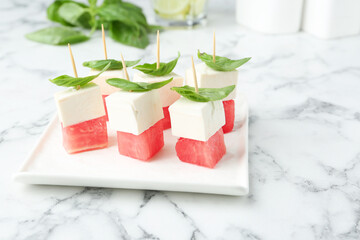 Tasty canapes with watermelon, feta cheese and basil on white marble table