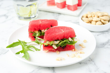 Tasty appetizer with watermelon, cashews and arugula on white marble table