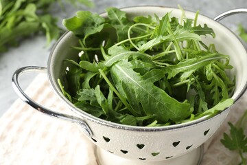 Fresh green arugula leaves in colander on table, closeup