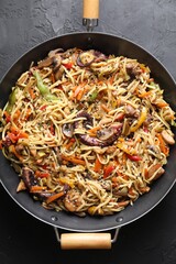Stir-fry noodles with sea food and vegetables in wok on dark textured table, top view