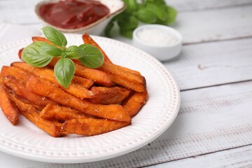 Sweet potato fries and basil on light wooden table, closeup