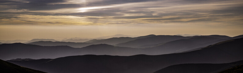 a panorama of the mountains at sunset, the fog covers the lowlands between the mountains that stretched to the very horizon, an incredibly beautiful sky painted as if with watercolor paints, the beaut