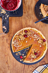Top view of pumpkin pie with pecans and cranberries lying on a black dish on a black wooden tray