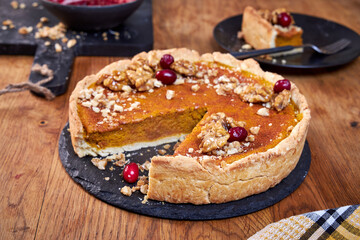Top view of pumpkin pie with pecans and cranberries lying on a black dish on a black wooden tray