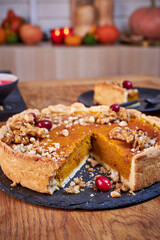 Top view of pumpkin pie with pecans and cranberries lying on a black dish on a black wooden tray