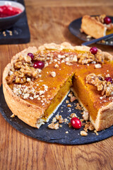 Side view of pumpkin pie with pecans and cranberries lying on a black dish on a black wooden tray