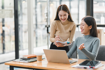 Collaborative women working together in modern office, sharing ideas and smiling while using laptop and notebook. Their positive energy enhances creative atmosphere.