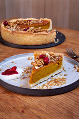 A slice of pumpkin pie with cream and cranberries rests on a ceramic plate on a wooden table