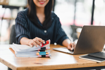 Efficient woman organizing documents while working on laptop in modern office. Her focused expression reflects productivity and professionalism.