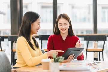 Two women collaborating in modern workspace, discussing ideas while using tablet. Their expressions convey enthusiasm and teamwork, highlighting productive atmosphere.