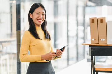 young woman in yellow sweater stands confidently in modern office, holding smartphone and smiling...