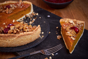 Top view of pumpkin pie with pecans and cranberries lying on a black dish on a black wooden tray