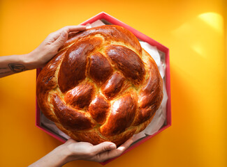Hands holding round fresh challah in a Magen David shaped box on a yellow background. Jewish New Year. Traditional aromatic pastries for the holiday