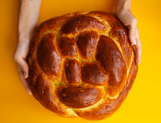 fresh homemade bread baked for the holiday - round challah in hands on a bright background
