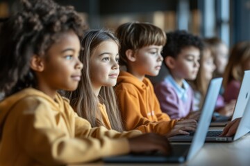 A group of children are sitting at a table with laptops open in front of them. They are all focused on their work, likely doing a school project or assignment. Scene is focused and studious