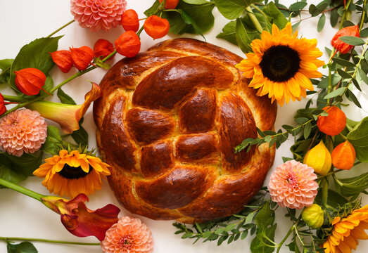 Fresh round challah on a white background with fresh flowers. Jewish traditional homemade aromatic pastries for the holiday