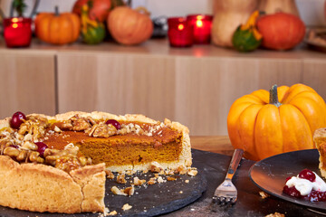 Side view of pumpkin pie with pecans and cranberries lying on a black dish on a black wooden tray
