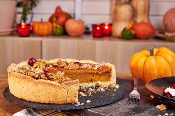 Side view of pumpkin pie with pecans and cranberries lying on a black dish on a black wooden tray