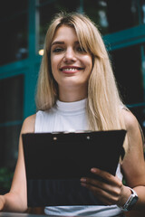 Cheerful woman with clipboard using laptop