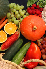 Round straw bag and various seasonal fruits and vegetables on dark background. Summer and fall produce. Top view.