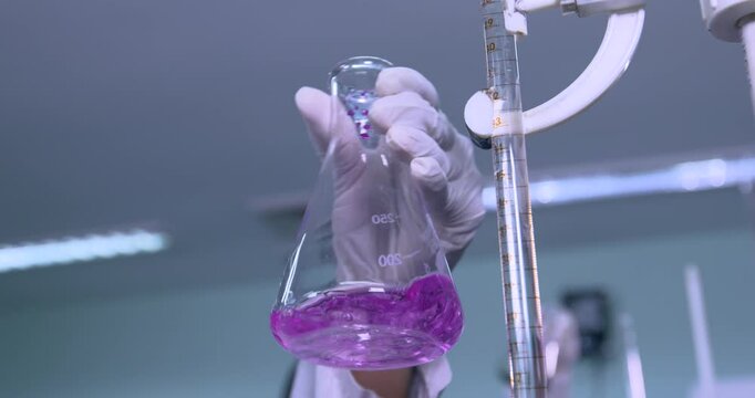 Chemical mixing, close up of a Scientist conducting science experiment in a beaker. flask titration with colorful pink chemical liquid in a laboratory with science lab equipments	