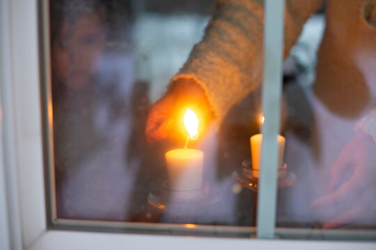 A person inside a house lights a candle seen through a frosty window on a cold day.