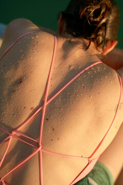 Close-up of a woman's sun-kissed back with wet sand particles adhering to her skin, and her wearing a pink crisscross strapped swimsuit.