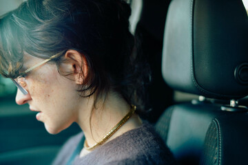 Profile view of a woman with glasses sitting in a car, looking downwards with a thoughtful expression.