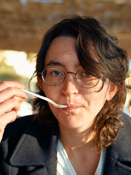 Woman enjoying a spoonful of food outdoors with sunlight illuminating her face.