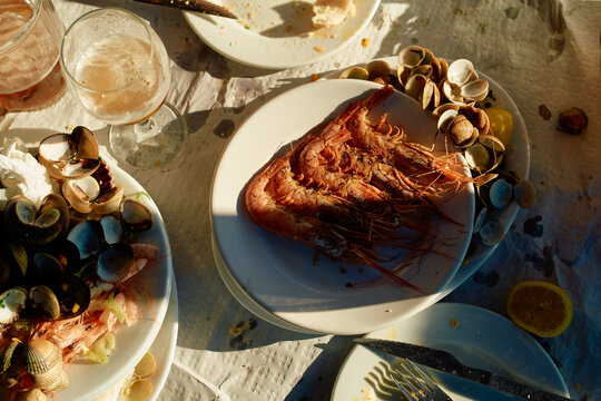 Evening light casts shadows on a table with seafood dishes and drinks during a meal.