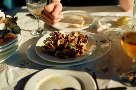 A close-up view of a table during a seafood meal, featuring a plate of clams, partially eaten food, and drinks under warm lighting.