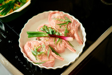 Fresh raw lamb chops garnished with spring onions and herbs on a white plate, ready to be cooked.